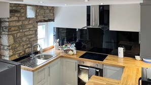 Een moderne keuken met een accentmuur van steen, een inbouwfornuis en een houten aanrecht.