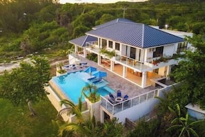 Ein zweistöckiges Haus mit Swimmingpool, umgeben von viel Grün.