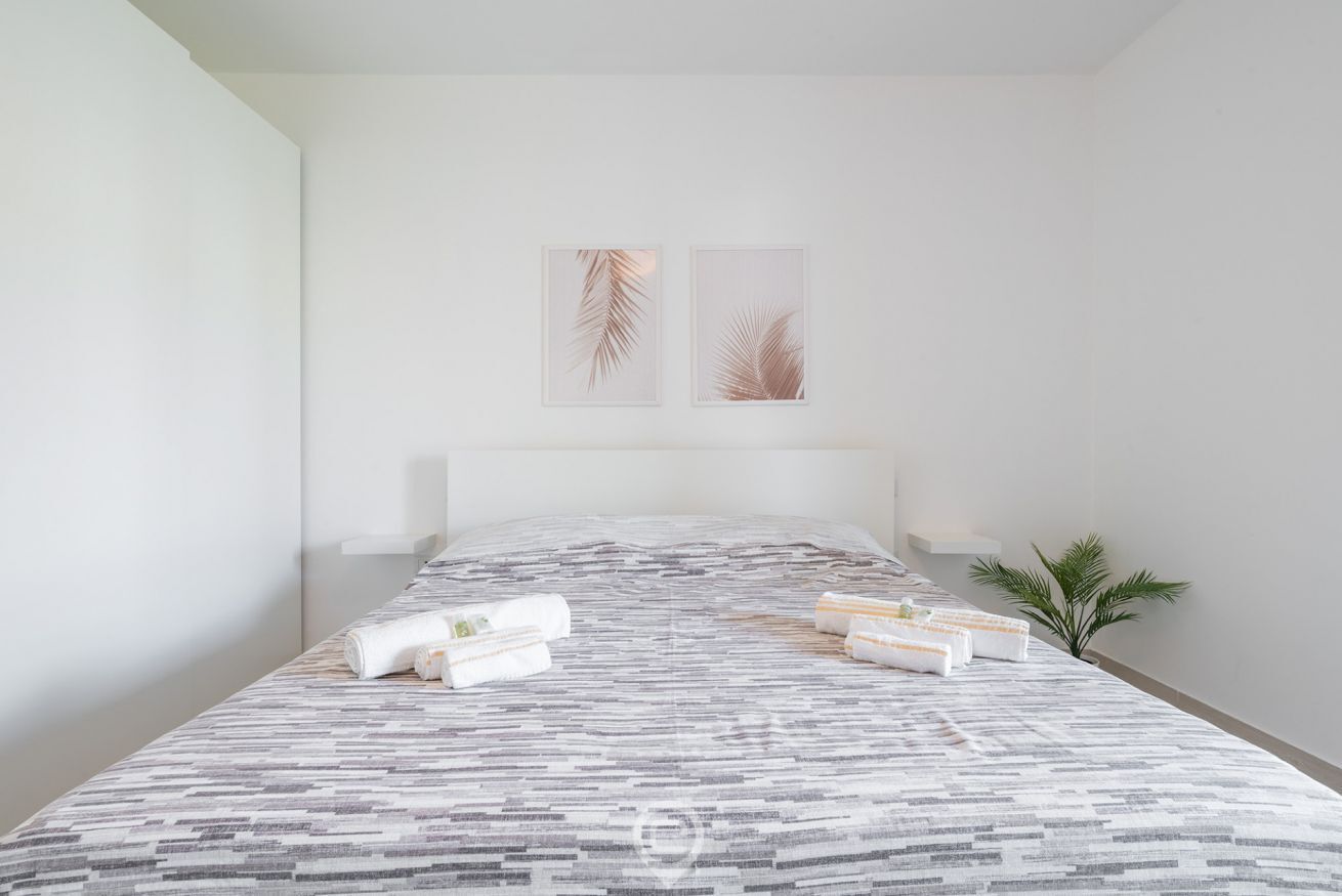 Una habitación de hotel moderna con una cama grande, toallas ordenadas y dos cuadros con hojas en la pared.