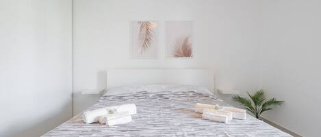 Una habitación de hotel moderna con una cama grande, toallas ordenadas y dos cuadros con hojas en la pared.