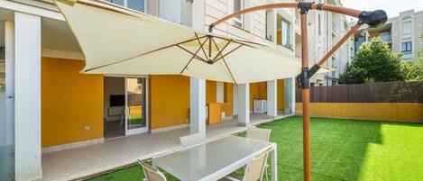 A patio with a table and chairs, a retractable awning, and a building with yellow walls and large windows.
