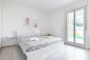 Et soveværelse med en seng, et lille natbord, en potteplante og en skydedør, der fører til en balkon.