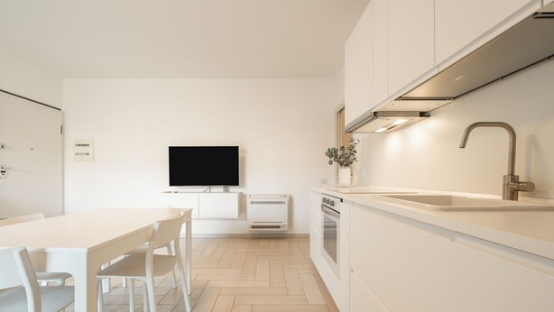 A modern kitchen with white cabinetry, a flat-screen TV, a built-in oven, and a stainless steel sink.