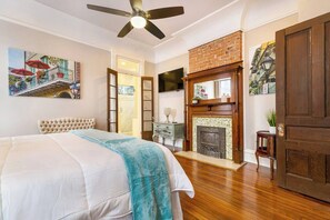 Un dormitorio con cama, ventilador de techo, chimenea y una puerta.