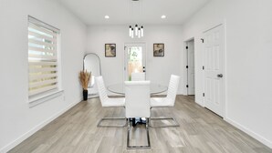 A modern dining area with a round table, white chairs, and pendant lighting. - Grand Luxé Retreat: Lux Home ★ GATED ★ FREE PARKING ★ Medical Center & NRG (Houston)