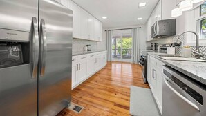 A modern kitchen with stainless steel appliances, white cabinetry, and a herringbone tile backsplash. - Picturesque Lakeside Luxury: Perfect Lush Getaway (Hampton)