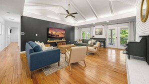 A spacious living room with a fireplace, a ceiling fan, and a large TV on the wall. - Picturesque Lakeside Luxury: Perfect Lush Getaway (Hampton)