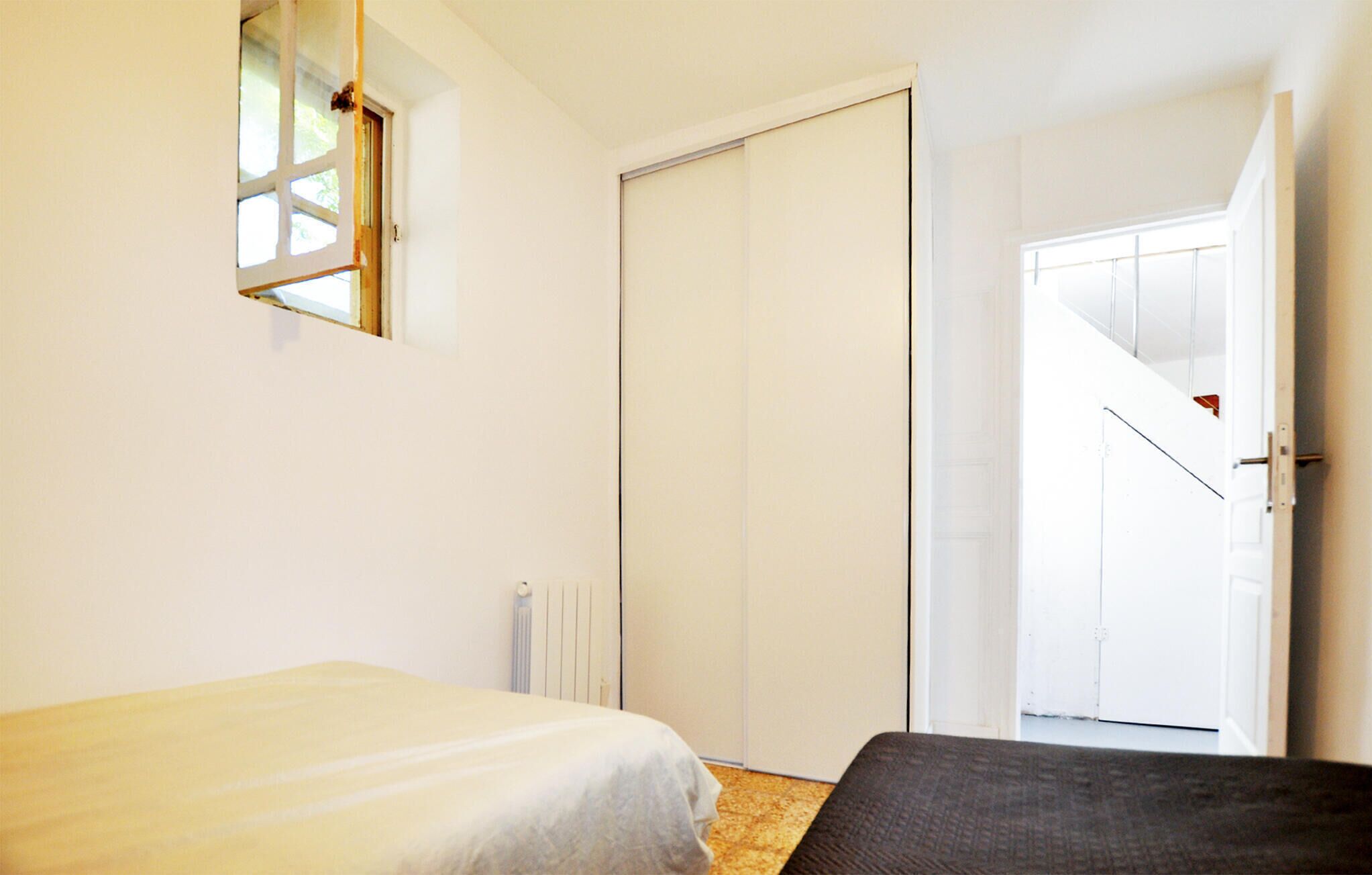 A bedroom with a bed, a radiator, a wardrobe, and a door leading to another room.
