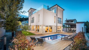 A modern two-story house with a swimming pool, outdoor seating, and a well-maintained garden.