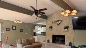 Una sala de estar con chimenea, ventilador de techo y televisión montada en la pared.