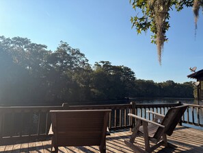A wooden deck with two chairs overlooking a calm body of water, surrounded by dense trees. - Two Story House with deck over the river (Karnack)