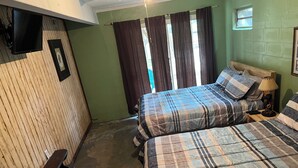 Una habitación con dos camas, un banco, un televisor y una ventana con cortinas.