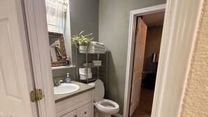 Un baño con inodoro, lavamanos y un estante con toallas y una planta.