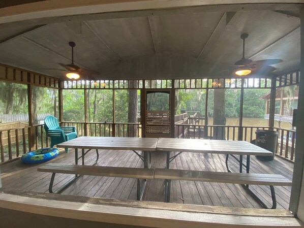 A covered outdoor area with a wooden deck, picnic tables, chairs, and a blue inflatable ring.