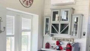 Un coin repas avec une table ronde et des chaises, une horloge au mur, et un espace cuisine avec des placards et des appareils électroménagers.