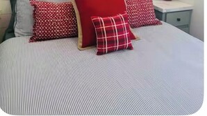 Un lit avec une literie à rayures et des oreillers rouges, une horloge murale et une petite table de chevet avec une lampe.