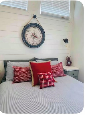 A bed with striped bedding and red pillows, a wall clock, and a small bedside table with a lamp. - Elk Mountain at Laney Lane  (Luna)