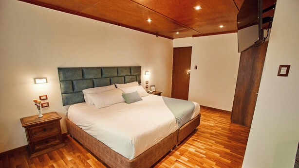 A bedroom with a wooden floor, a bed with a green headboard, two bedside tables, and a nightstand. - Inti Tampu Inn (Cusco)