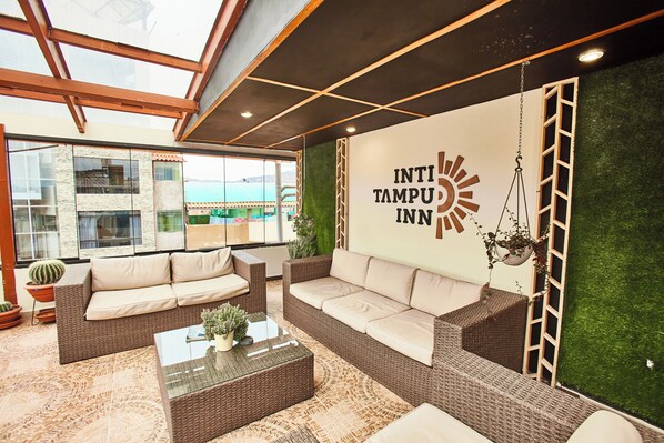 A modern interior with wicker furniture, a glass coffee table, and a wall-mounted sign for INTI TAMPU INN.