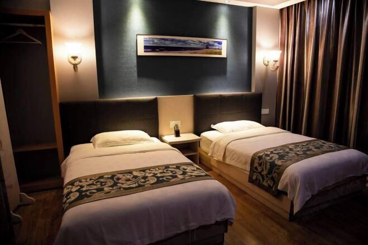 A hotel room with two beds, a dark wall with a framed picture, and a wooden floor.