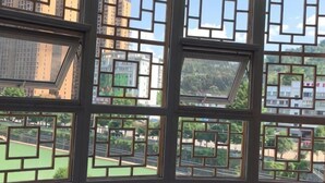 A view through a window with geometric patterns, revealing a green outdoor area and buildings in the background. - Xuan En Jingyi Sunshine Inn (Xuan'en)