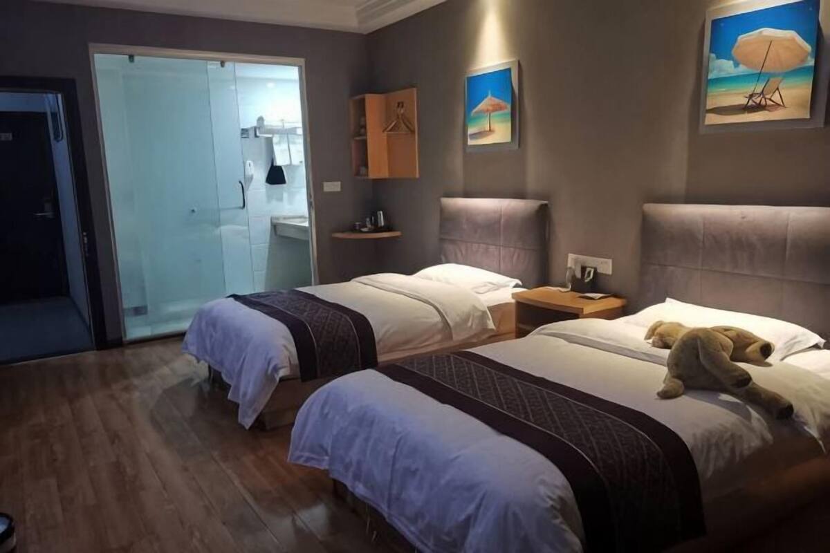 A hotel room with two beds, a wardrobe, a bathroom, and a painting on the wall.