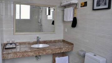 Un baño con un espejo grande, un lavamanos y un inodoro. Hay toallas y un secamanos en la pared.