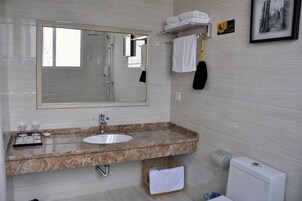 Un baño con un espejo grande, un lavamanos y un inodoro. Hay toallas y un secamanos en la pared.