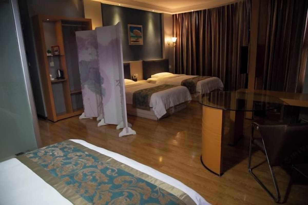 Quarto de hotel com duas camas, uma escrivaninha, uma cadeira, um guarda-roupa e um quadro na parede.