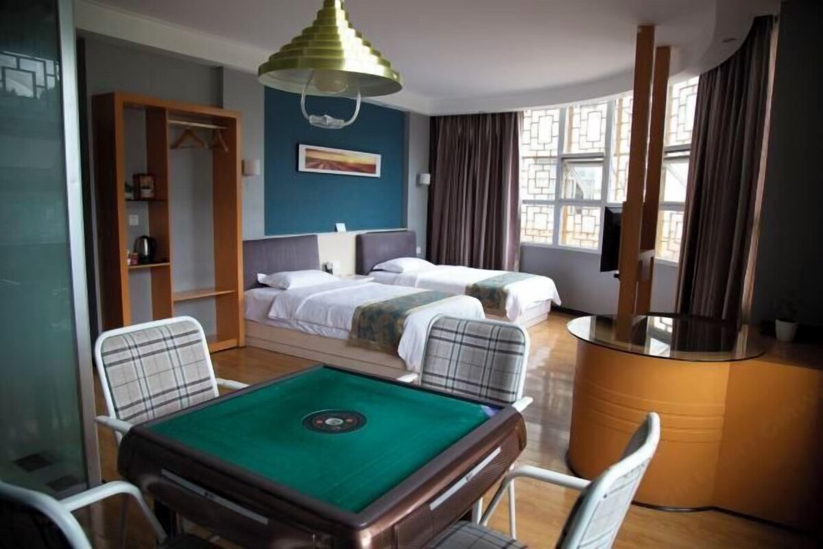 Une chambre d’hôtel avec deux lits, une table de billard, un bureau et une grande fenêtre avec des rideaux.