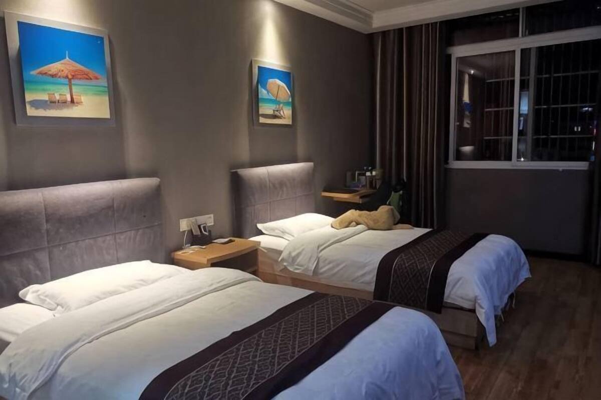 A hotel room with two beds, a nightstand, a window with curtains, and artwork on the walls.