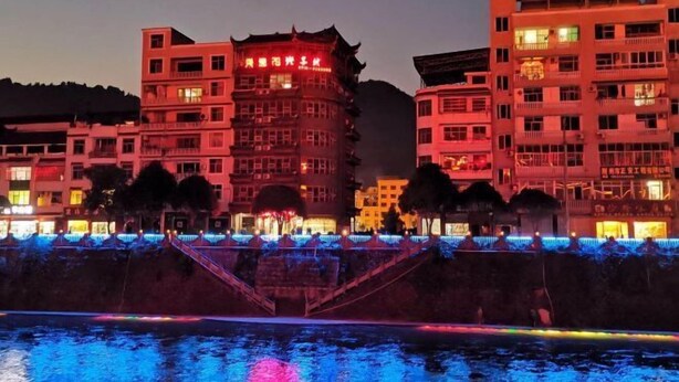 A multi-story hotel with illuminated signage, a water feature in the foreground, and a staircase leading to the upper levels. - Xuan En Jingyi Sunshine Inn (Xuan'en)