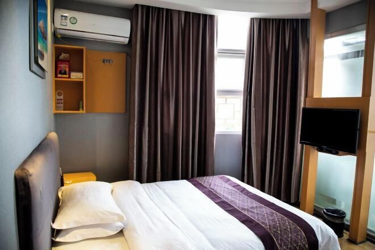 Une chambre d’hôtel avec un lit, des rideaux, une télévision et une étagère avec quelques objets.