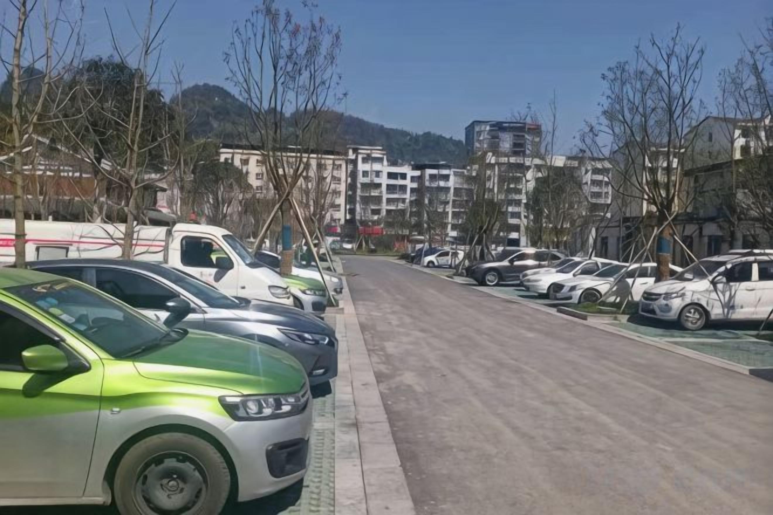 A parking lot with multiple cars, a clear sky, and buildings in the background.