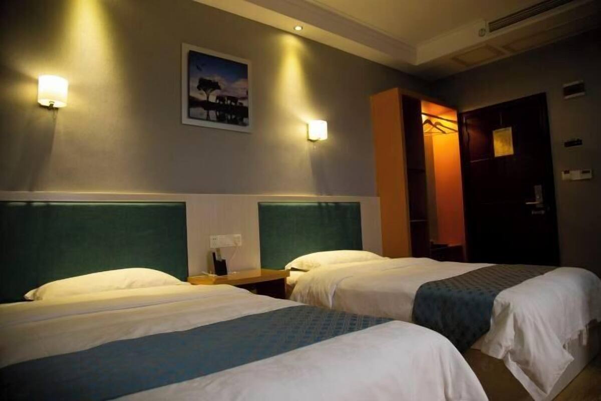 A hotel room with two beds, each with a headboard, a nightstand, and a wall-mounted lamp.