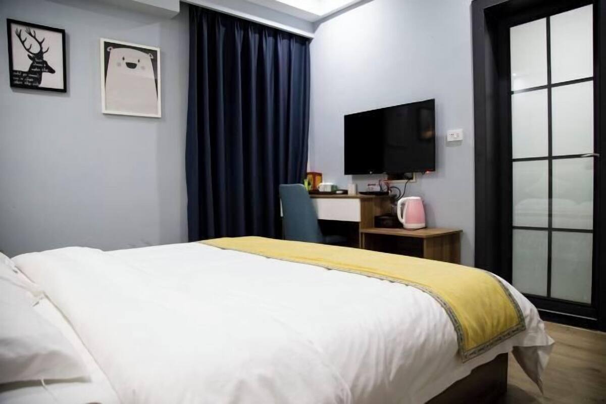 A hotel room with a bed, a desk with a computer, a TV, and a window with curtains.