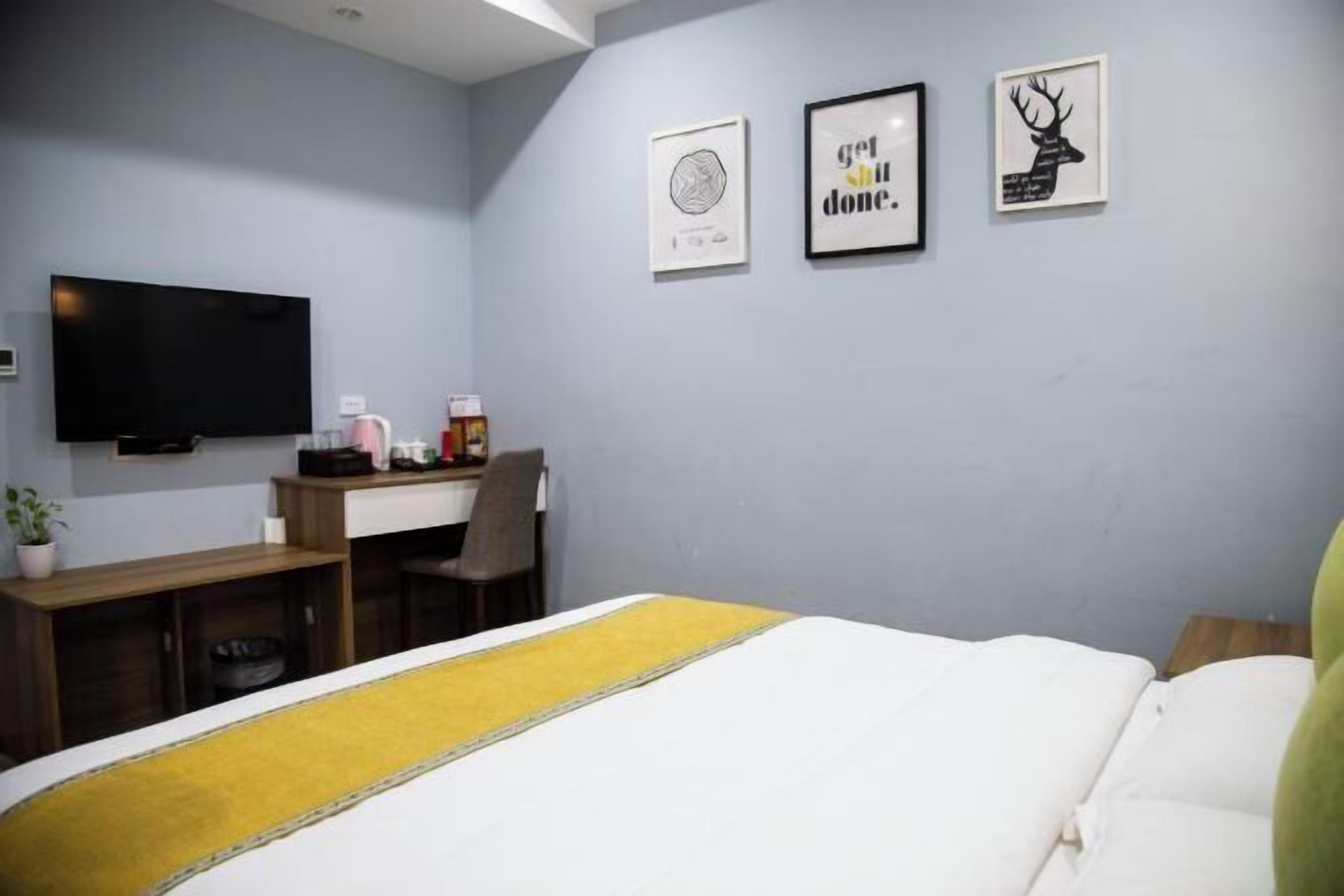 A hotel room with a bed, a desk, a chair, a TV, and artwork on the wall.