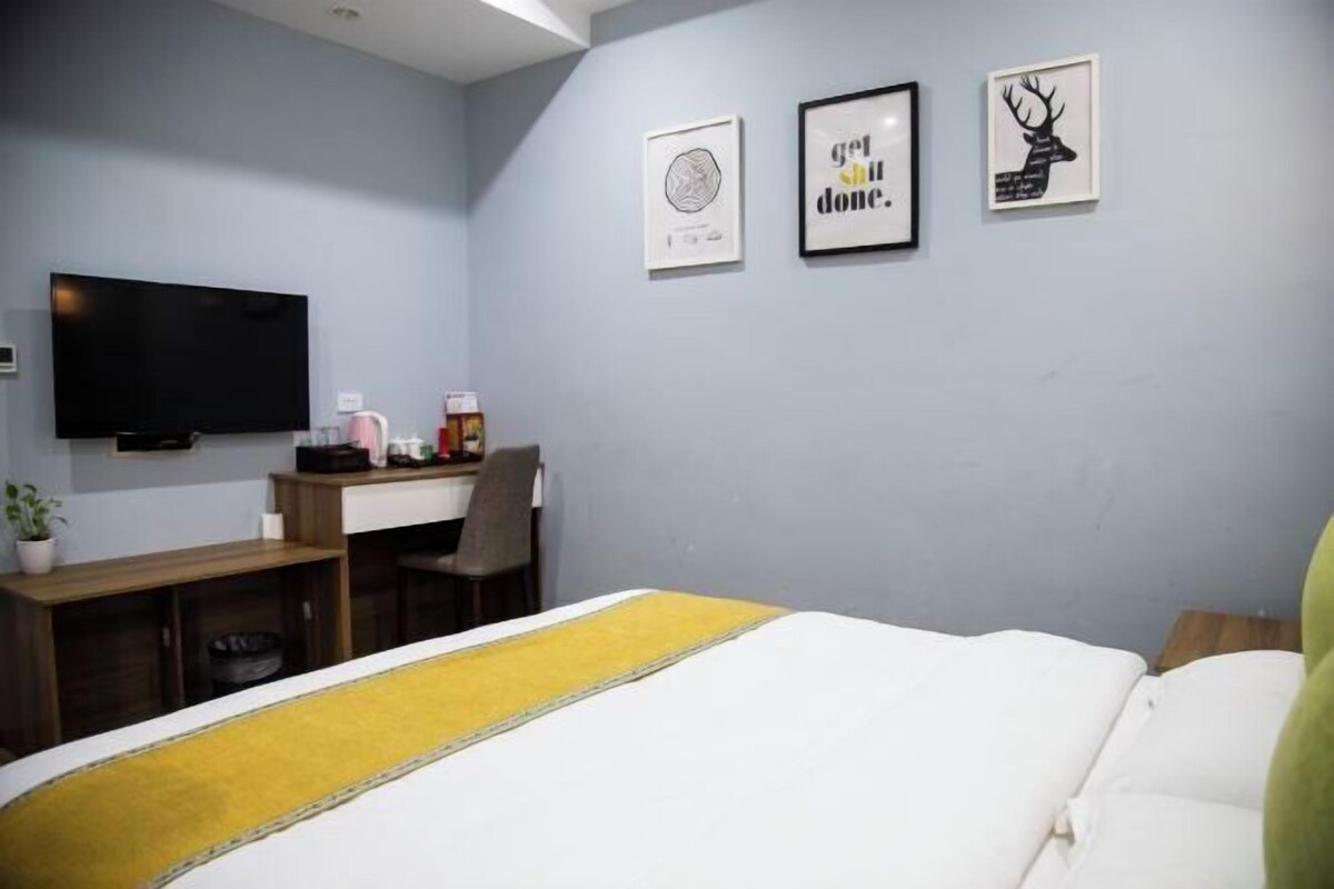 Une chambre d’hôtel avec un lit, un bureau, une chaise, une télévision et des œuvres d’art accrochées au mur.