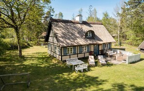 Ein traditionelles Fachwerkhäuschen mit Strohdach, einer kleinen Veranda mit Sitzgelegenheit und einem Schild mit dem Namen "Husum".