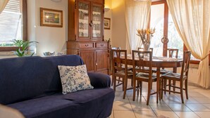 A living room with a dark blue sofa, wooden dining table, and chairs. There is a cabinet with glass doors and a chandelier above the table. - Villa Ontanelli - 500mt from the sea (Marciana Marina)