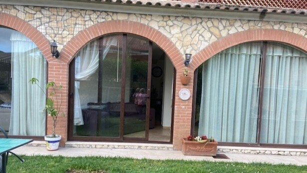 Ein Haus mit einer Stein-Fassade, großen Glasüren und einem kleinen Garten mit Tisch und Blumentöpfen.