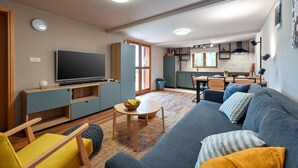 Moderni olohuone, jossa on sohva, televisio sekä ruokailutila pöytineen ja tuoleineen.