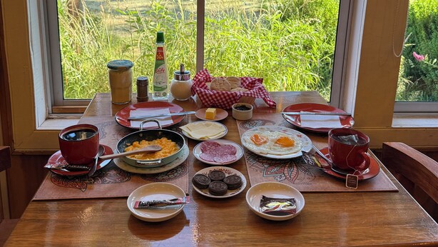 Taula de l'esmorzar amb diferents plats, una tassa de cafè i vista a un paisatge de muntanya a través d'una finestra.