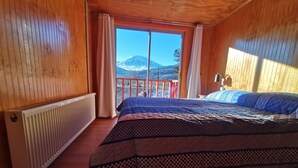 Habitació de cabana de fusta amb un llit, una finestra amb cortines i vista a una muntanya.