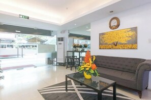 A lobby with a sofa, a coffee table with flowers, and a painting on the wall. - RedDoorz @ Tesoro Apartments Ermita Manila (Manila)