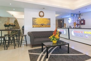 A hotel lobby with a reception desk, a grey sofa, a coffee table with flowers, and a Christmas tree. - RedDoorz @ Tesoro Apartments Ermita Manila (Manila)