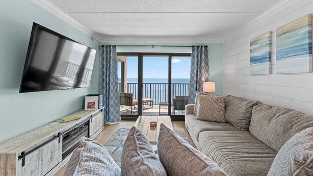 A living room with a flat-screen TV, a sofa, a coffee table, and a view of the balcony. - Oceanfront Oasis | Indoor Pool | Hot Tub | Deck (Ocean City)