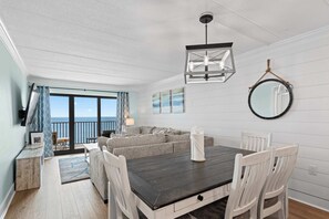 A dining area with a dark wooden table, white chairs, a round mirror, and a view to the outside.