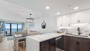 A modern kitchen with marble countertops, dark cabinets, and a view to the outside. - Oceanfront Oasis | Indoor Pool | Hot Tub | Deck (Ocean City)