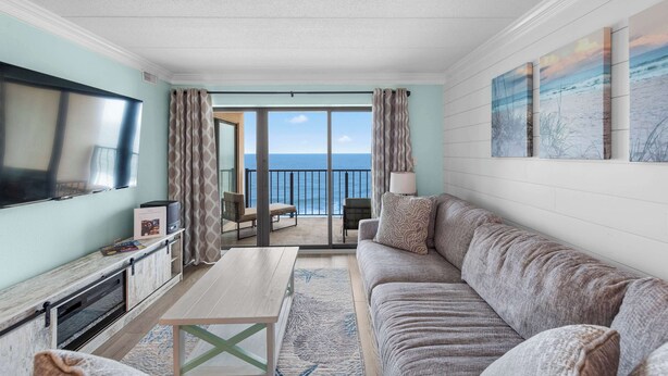 Een woonkamer met een televisie, bank, bijzettafeltje en uitzicht op de oceaan vanaf een balkon.